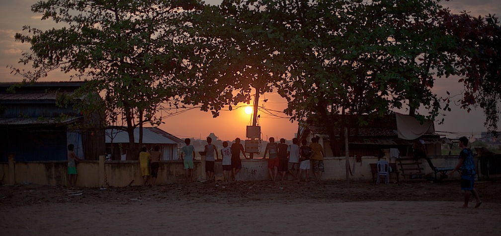 Kids watching the sun set as someone shags the ball from the lake.